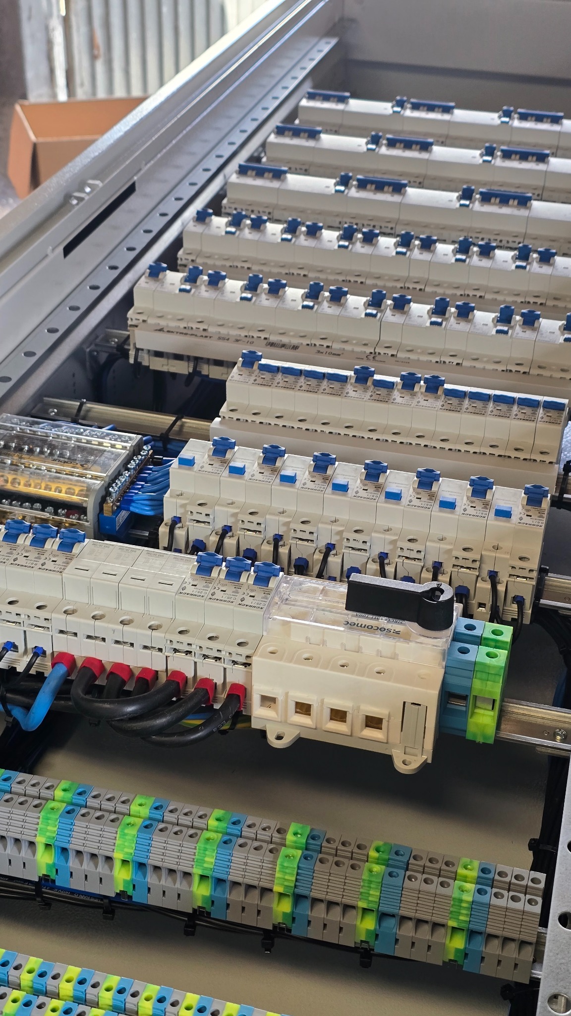 Rozdzielnica elektryczna z zabezpieczeniami nadprądowymi i listwami zaciskowymi, widoczne przewody w izolacji niebieskiej, czarnej i czerwonej. Profesjonalna instalacja.