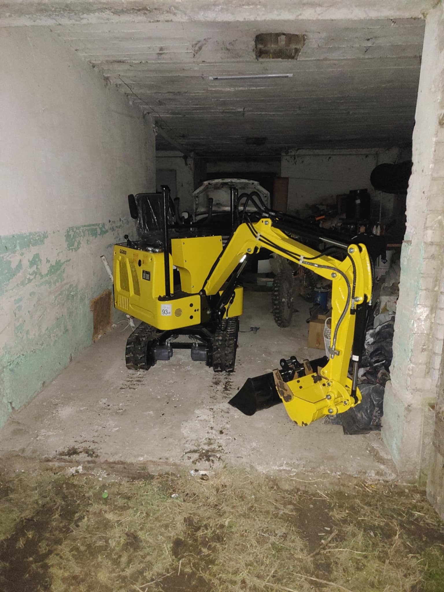 Żółta mini koparka GG800 na gąsienicach wewnątrz budynku z surowym wykończeniem, z widocznym osprzętem i łyżką, gotowa do pracy.