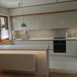 Białe fronty akrylowe w połączeniu z elementami drewnopodobnymi, blat z płyty mineralno-akrylowej