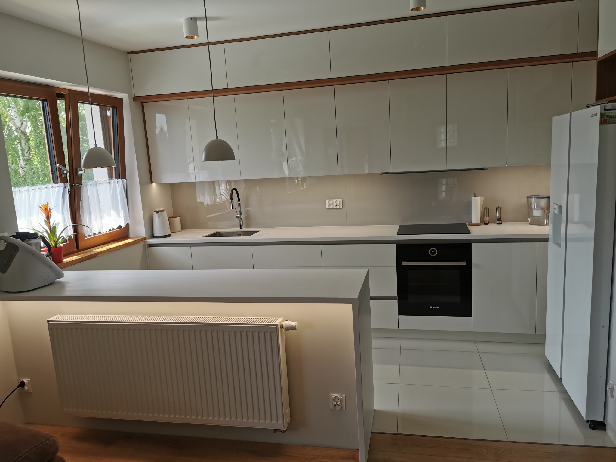 Białe fronty akrylowe w połączeniu z elementami drewnopodobnymi, blat z płyty mineralno-akrylowej