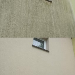 Firma Usługowo-Handlowa MK Clean Pressure Mariusz Kopala - Elewacja budynku przed i po czyszczeniu, widoczne różnice w kolorze i usunięte zabrudzenia. Okno z białą ramą w kadrze.