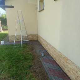 Firma Usługowo-Handlowa MK Clean Pressure Mariusz Kopala - Elewacja domu z dekoracyjnym kamieniem i kostką brukową, drabina oparta o ścianę, przygotowania do prac na zewnątrz budynku.