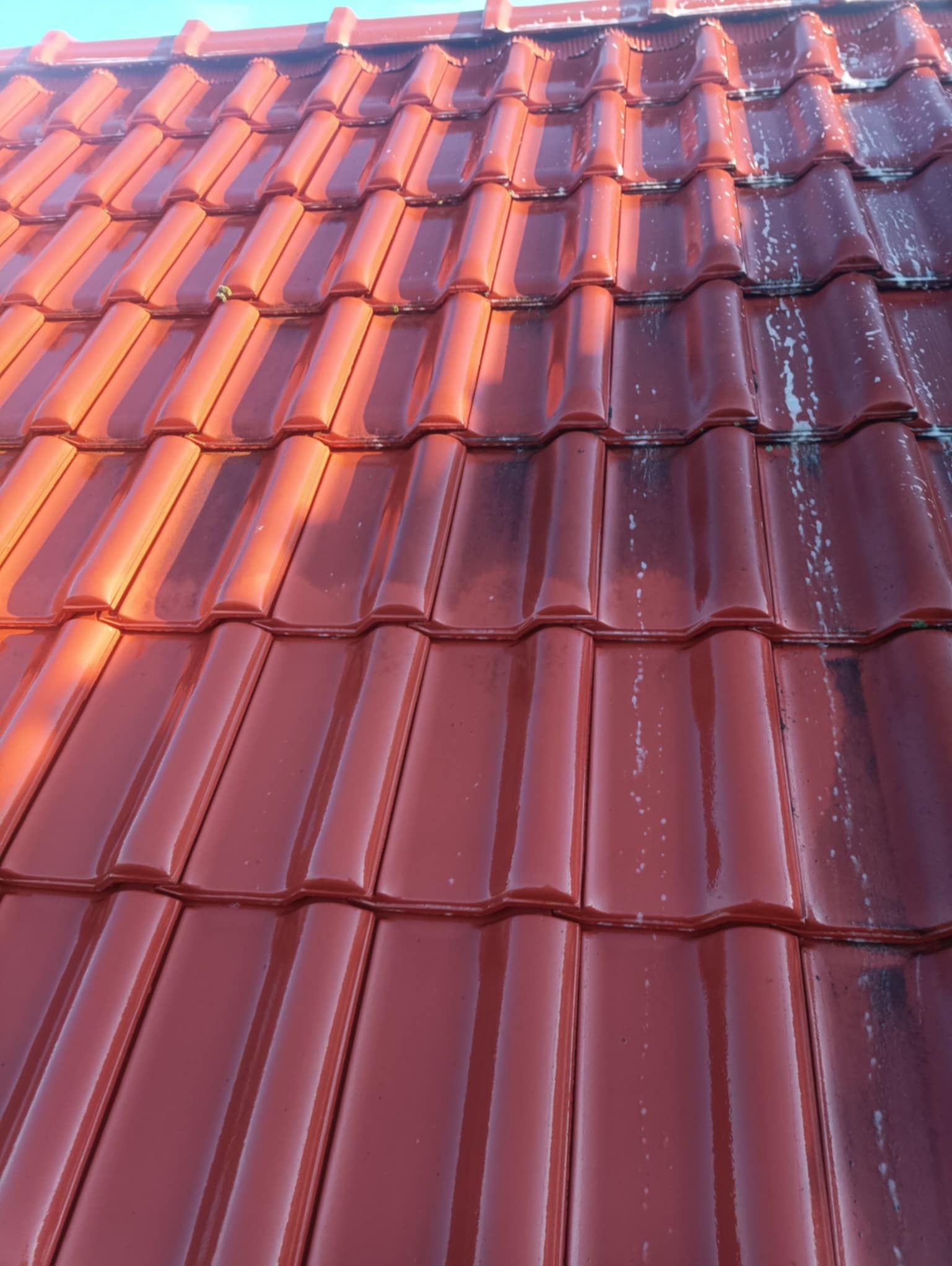 Czerwona dachówka ceramiczna, częściowo umyta, z widocznymi smugami wody i pozostałościami brudu. Kontrast czystej i zabrudzonej powierzchni.