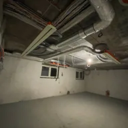 Surowy stan: instalacje elektryczne i wentylacyjne pod sufitem w nowym pomieszczeniu z oknami. Widoczne kable, rury wentylacyjne i elementy montażowe.