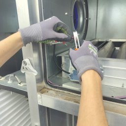 Sergei Redihin - Prace montażowe wewnątrz metalowej obudowy wentylatora. Widoczne dłonie w rękawicach ochronnych, przewody i elementy instalacji. W tle wentylator.