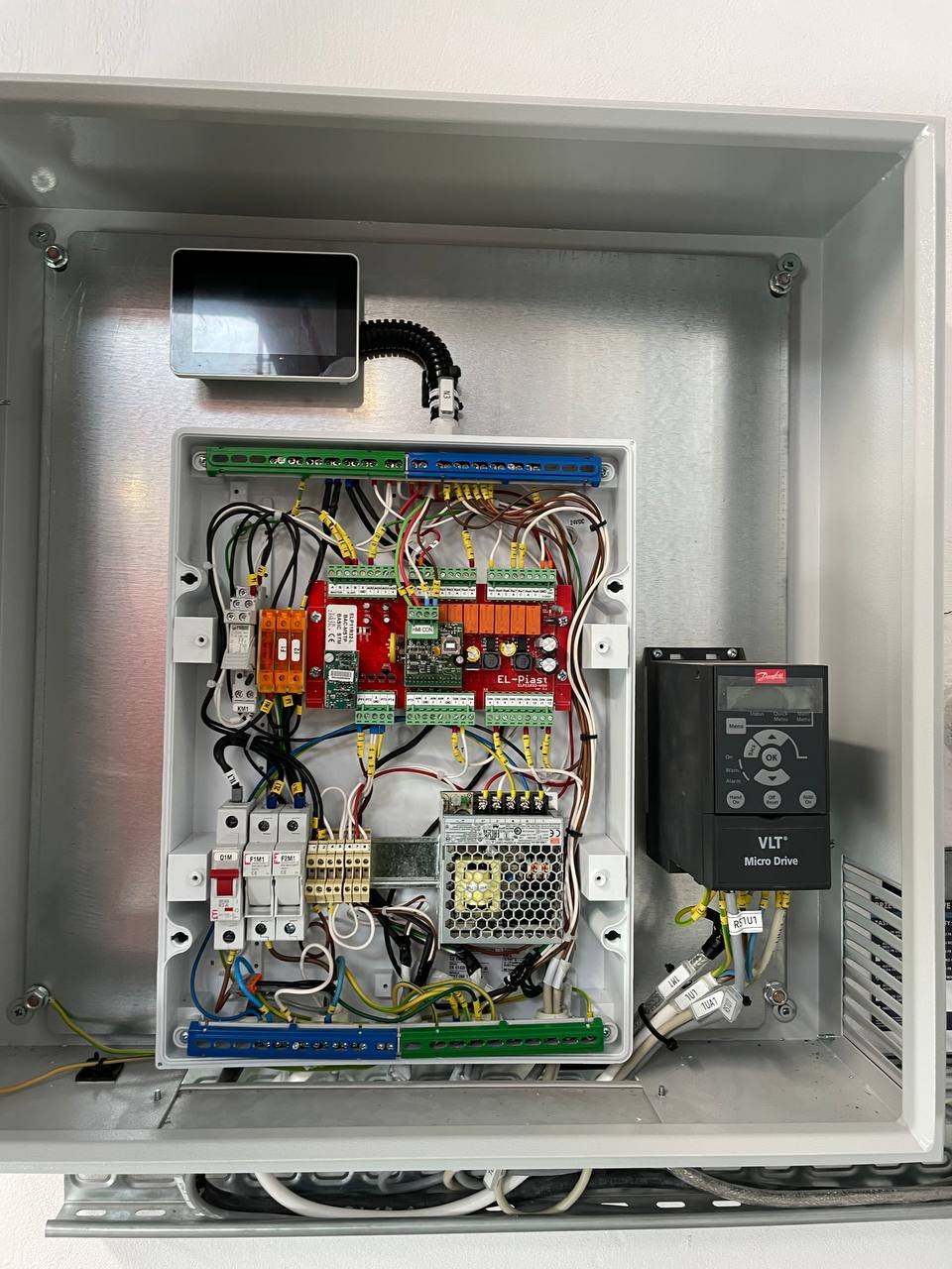 Otwarta szafa sterownicza z modułem sterującym EL-Piast, zasilaczem impulsowym i falownikiem Danfoss VLT Micro Drive. Widoczne okablowanie i elementy zabezpieczające.