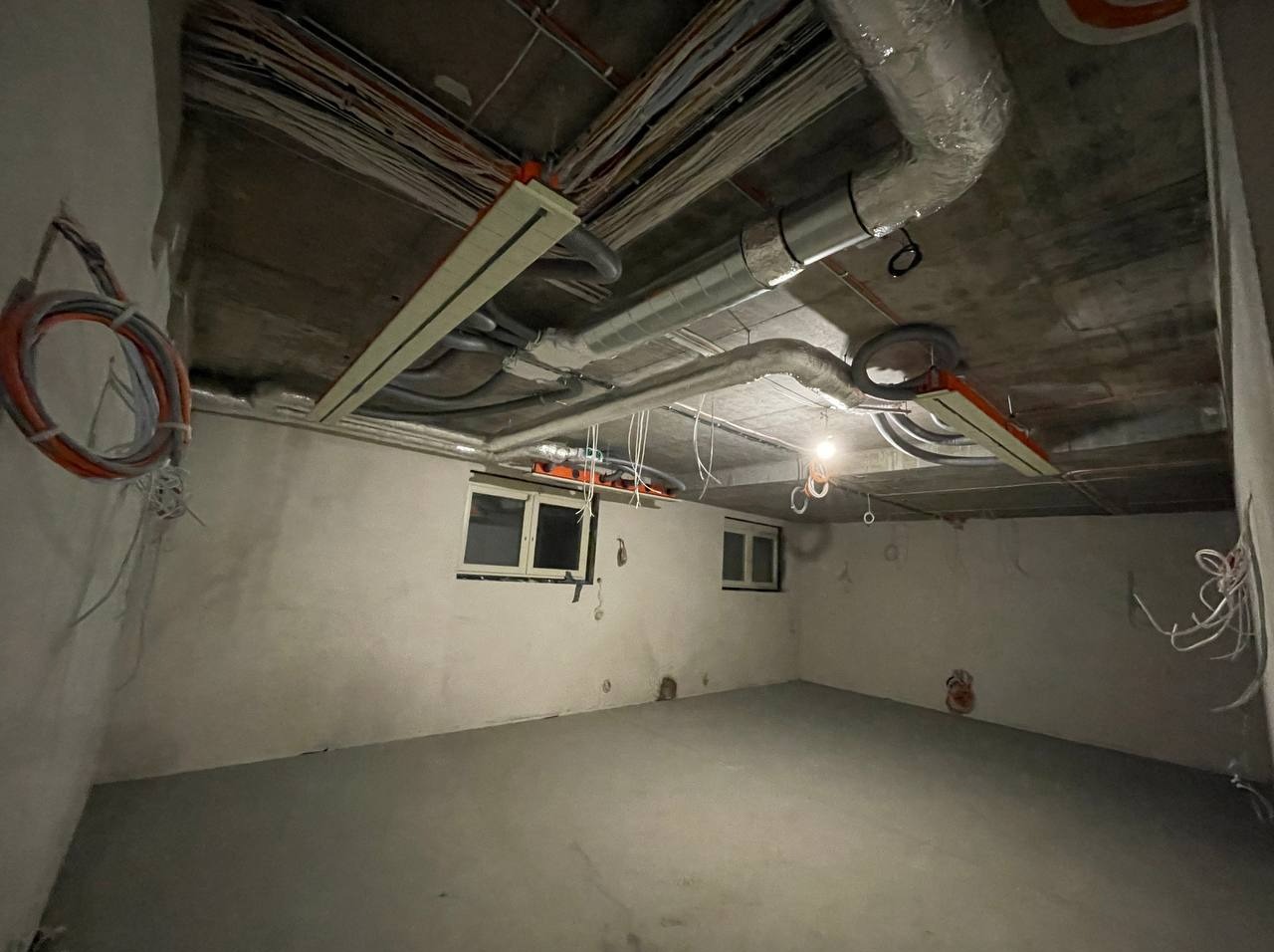 Surowy stan: instalacje elektryczne i wentylacyjne pod sufitem w nowym pomieszczeniu z oknami. Widoczne kable, rury wentylacyjne i elementy montażowe.