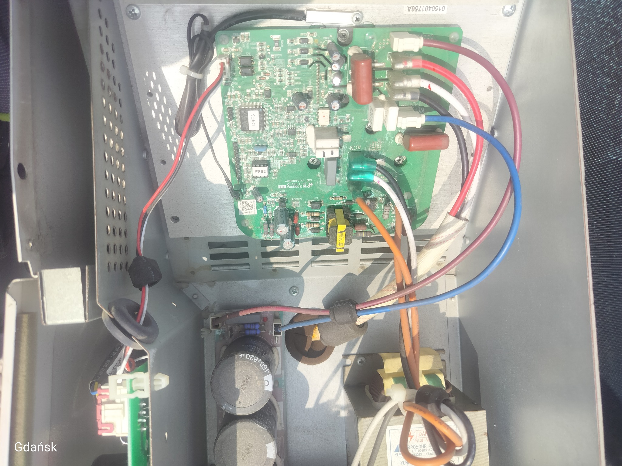 Otwarta obudowa urządzenia z widoczną płytą sterującą i okablowaniem. Elementy elektroniczne, kondensatory i złącza przewodów wewnątrz metalowej skrzynki.