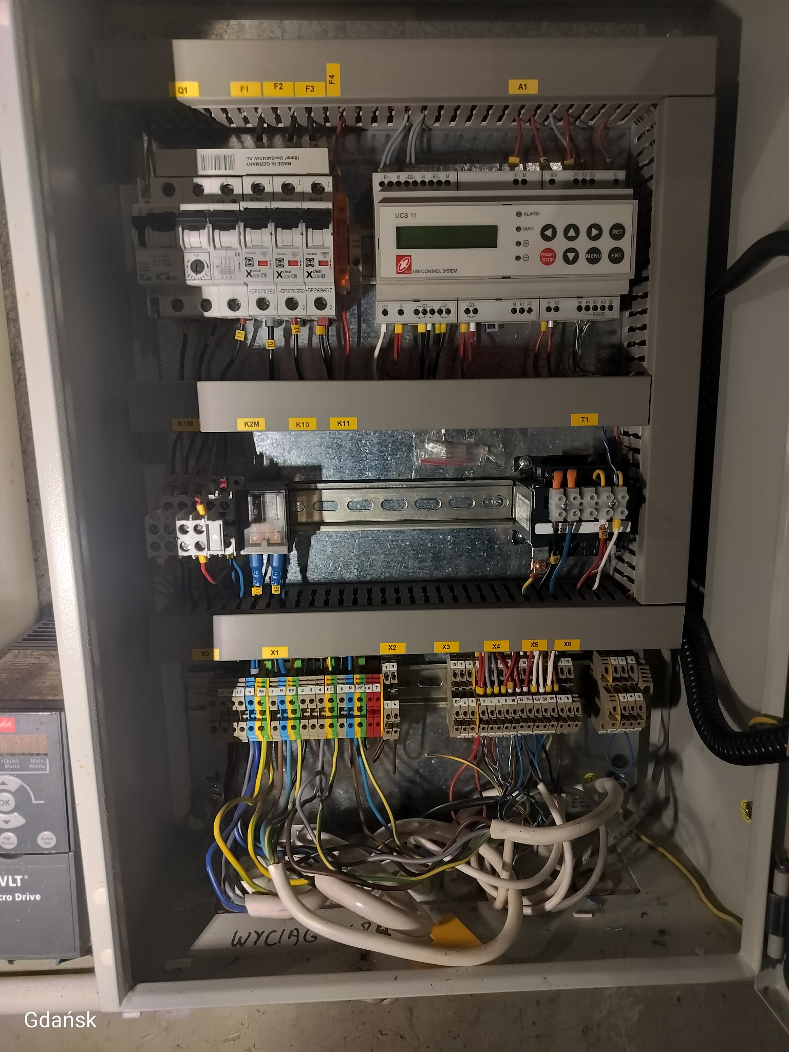 Rozdzielnica elektryczna z okablowaniem, widoczne bezpieczniki, sterownik Uni Control System UCS 11 i liczne złącza. Białe przewody ułożone na dnie szafy.