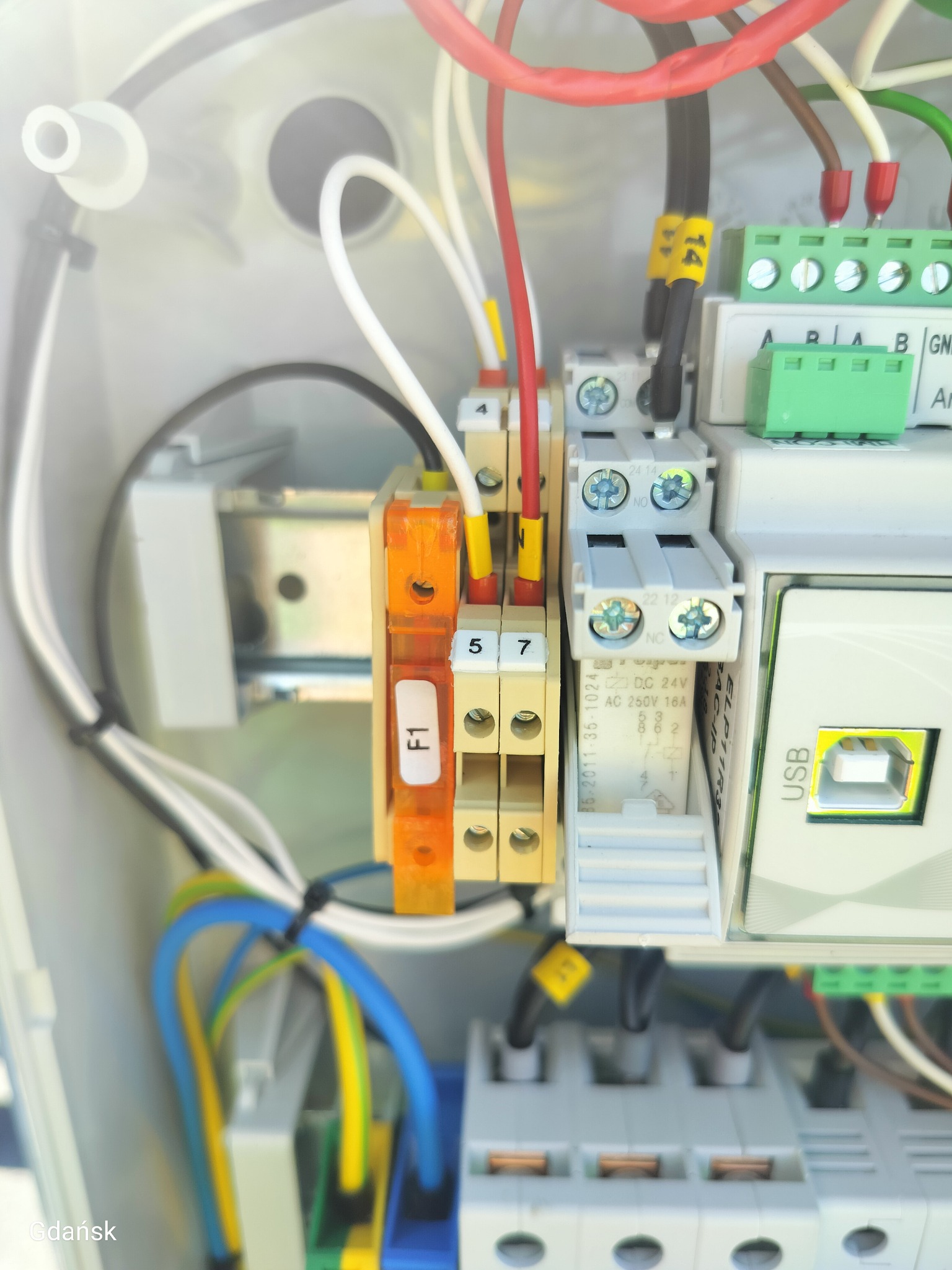 Szczegółowe zbliżenie na panel elektryczny z okablowaniem, bezpiecznikami i złączami USB. Widoczne oznaczenia na przewodach i elementach panelu.