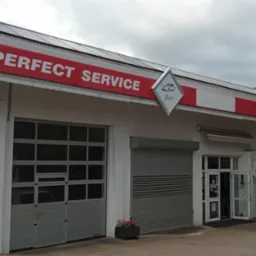 Fasada budynku warsztatu samochodowego 'Perfect Service Gold' z widocznymi bramami wjazdowymi i logo firmy. Na dachu panele solarne.