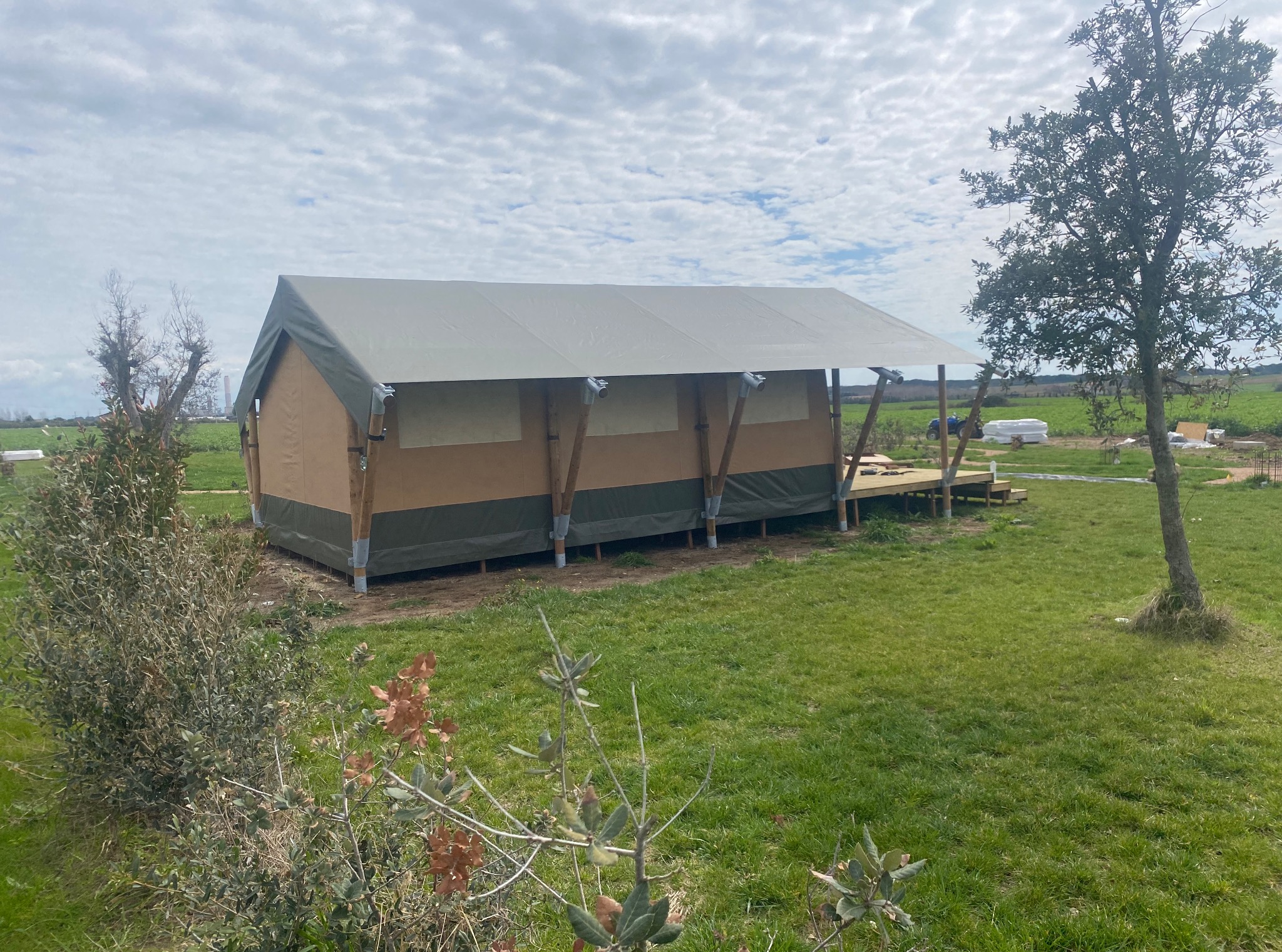 Gotowa konstrukcja altany z jasną plandeką, widoczna z zewnątrz na tle zielonego trawnika i błękitnego nieba z chmurami.