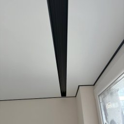 Andrei Malyshka Sufity napinane Pawbud - Biały sufit z czarną listwą dekoracyjną w nowocześnie wykończonym wnętrzu w Warszawie. Minimalistyczny design, widok z dołu.