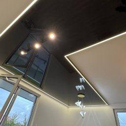 Andrei Malyshka Sufity napinane Pawbud - Nowoczesny, czarny sufit z oświetleniem LED wzdłuż krawędzi, nietypowe okno dachowe i designerska lampa wisząca. Widok z dołu, drabina w rogu pokoju.