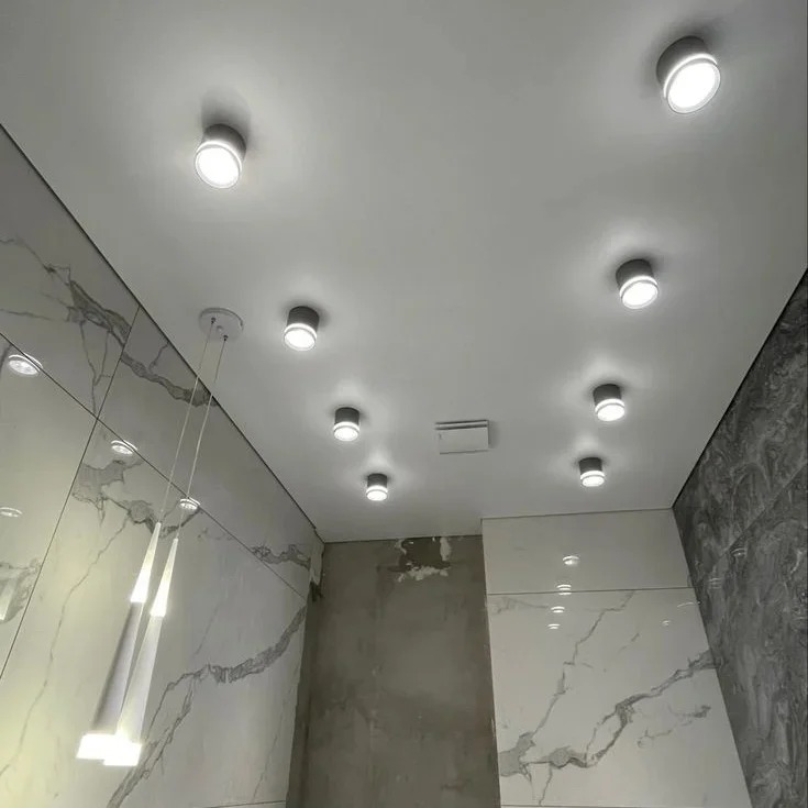 Biały sufit z równomiernie rozmieszczonymi punktowymi lampami LED, marmurowe ściany i wisząca lampa, nowoczesny design wnętrza łazienki.
