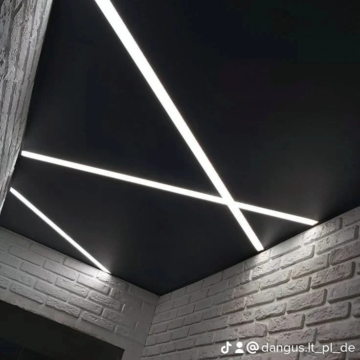 Nowoczesny sufit napinany w kolorze czarnym z wbudowanym oświetleniem LED, tworzącym geometryczny wzór. Ściany wykończone białą cegłą.