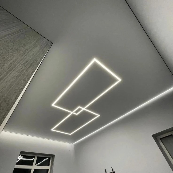 Nowoczesny pokój z białym sufitem, na którym umieszczono geometryczne, podświetlane prostokąty. Minimalistyczny design, sufit napinany z oświetleniem LED.