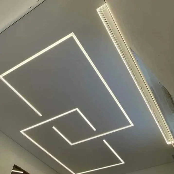 Nowoczesny sufit z podświetleniem LED w geometryczne wzory, oświetlenie liniowe przy ścianie. Minimalistyczny design wnętrza.
