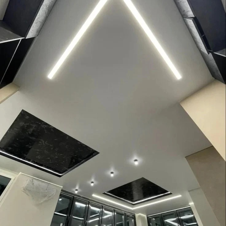 Nowoczesny sufit z podwieszanymi panelami w czarnym kolorze i oświetleniem LED, tworzącym geometryczny wzór. Widok z dołu ukazuje detale wykończenia.