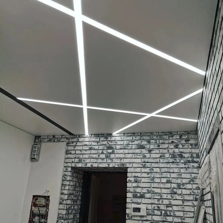 Biały sufit z liniowym oświetleniem LED w aranżacji z ceglaną ścianą i widoczną instalacją elektryczną. Nowoczesny design wnętrza.