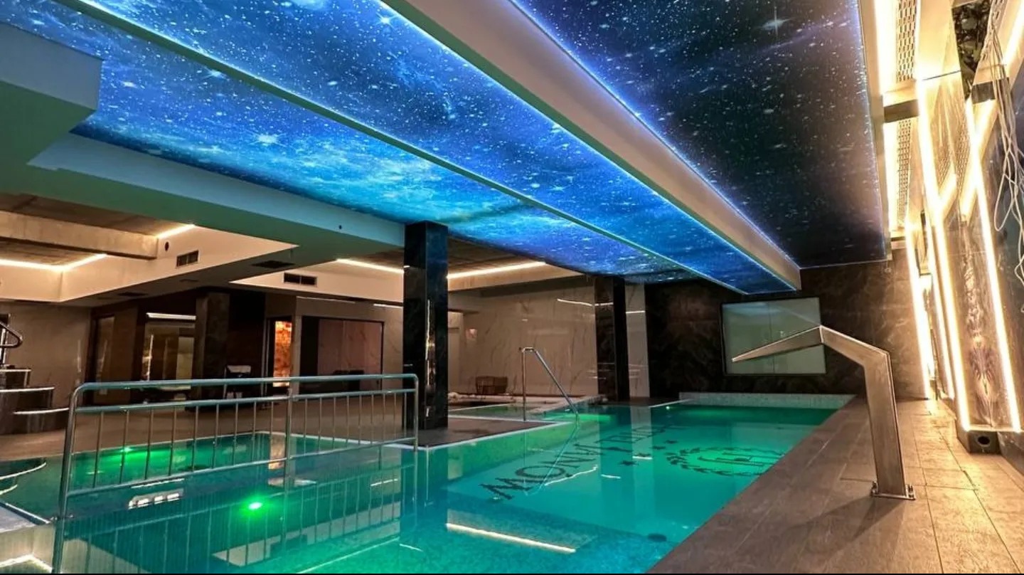 Sufit napinany z motywem kosmosu nad basenem w Warszawie. Nowoczesne oświetlenie, marmurowe wykończenie, elegancki design. Realizacja.