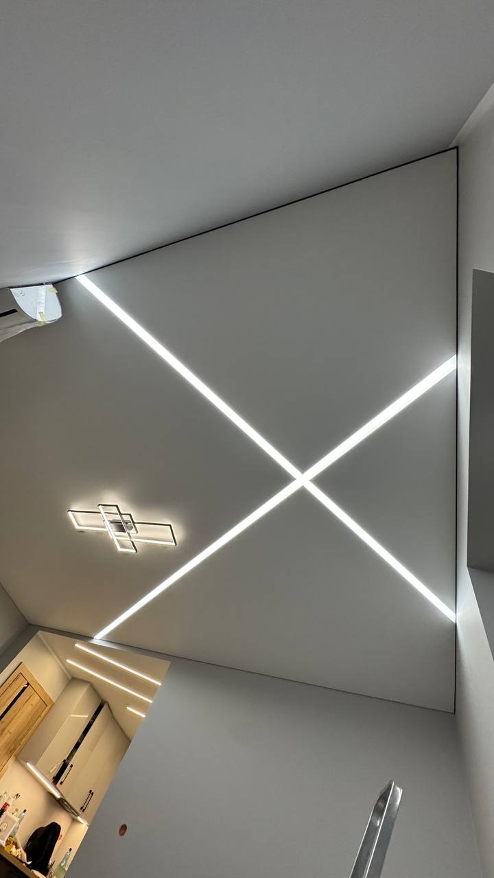 Nowoczesny sufit z podświetleniem LED w kształcie krzyża i designerską lampą. Widok z dołu, podkreślający geometrię i minimalistyczny styl wnętrza.