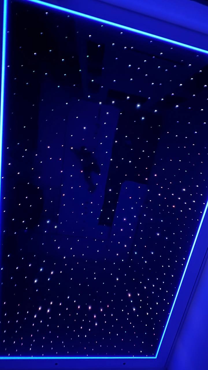 Niebieski sufit z efektem gwiazd, obramowany neonowym światłem. Widoczne ciemne elementy konstrukcyjne w tle, dodające głębi i unikalnego charakteru aranżacji.