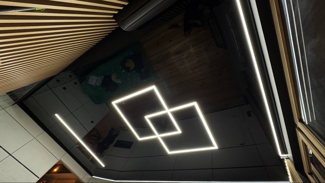 Błyszczący, czarny sufit z geometrycznym oświetleniem LED w kształcie dwóch kwadratów, drewniane panele na ścianie, nowoczesny design wnętrza.