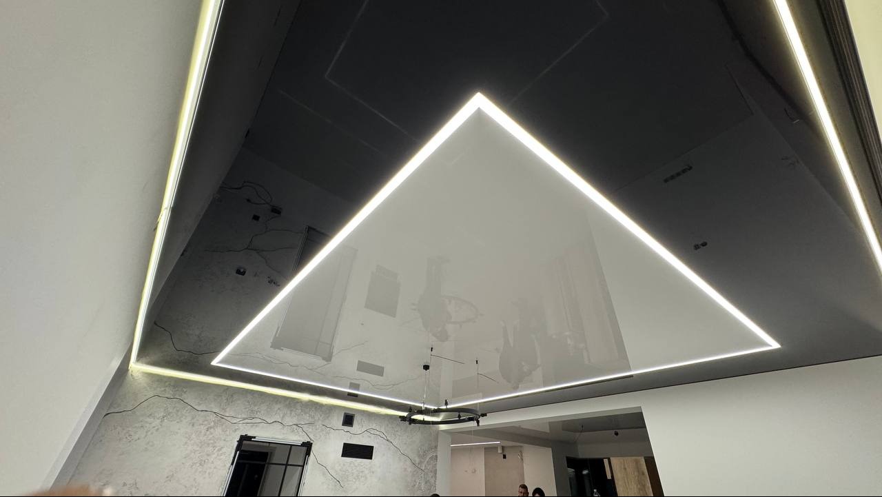 Nowoczesny, czarno-biały sufit z trójkątnym, podświetlanym panelem i listwami LED. Minimalistyczny design z widocznym oświetleniem i elementami dekoracyjnymi na ścianach.