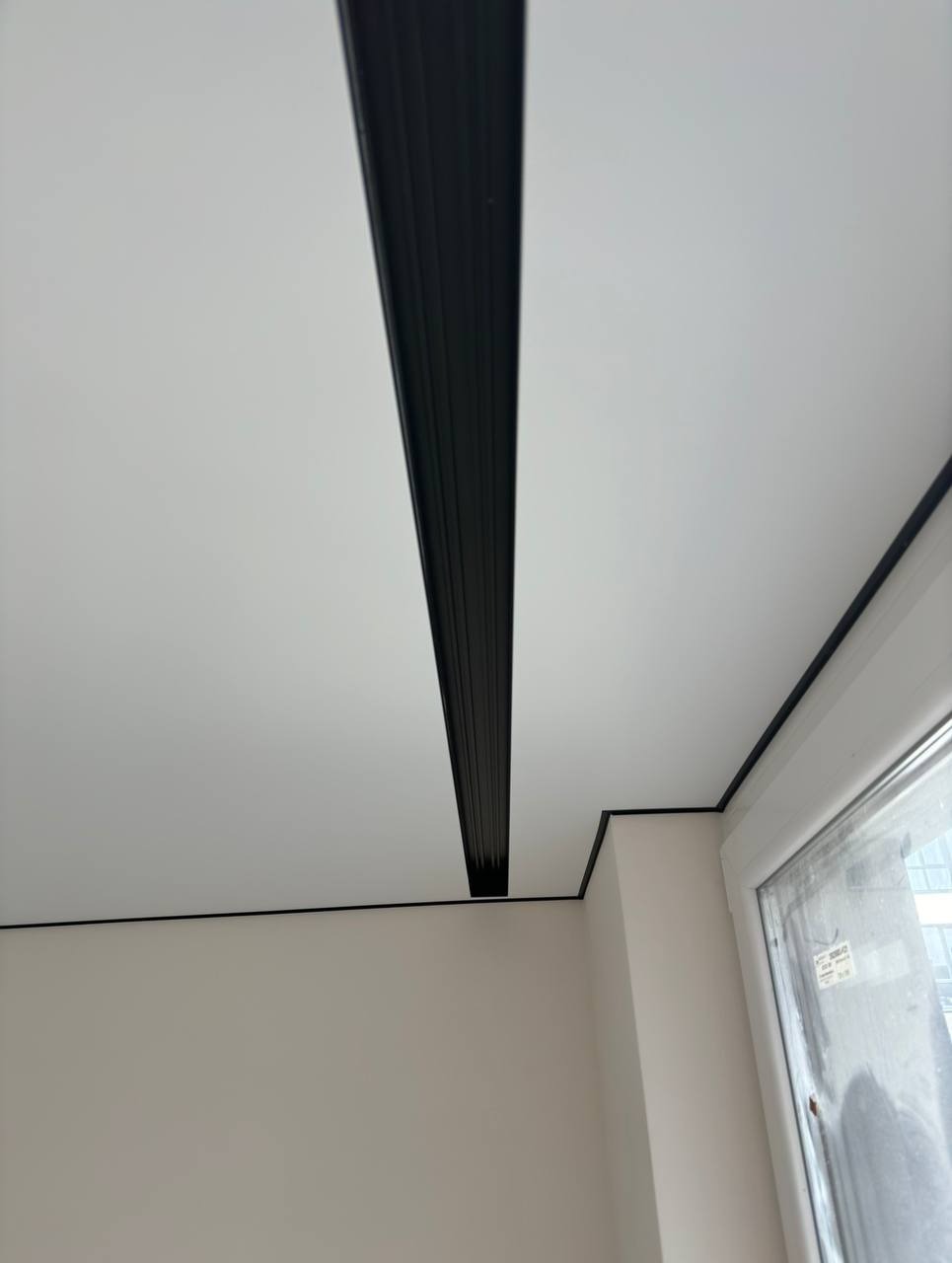 Biały sufit z czarną listwą dekoracyjną w nowocześnie wykończonym wnętrzu w Warszawie. Minimalistyczny design, widok z dołu.