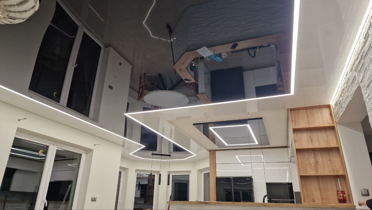 Błyszczący, czarny sufit z oświetleniem LED w nowoczesnym wnętrzu. Widoczne odbicie kuchni i okien, tworzące iluzję przestrzeni. Geometryczne wzory świetlne.