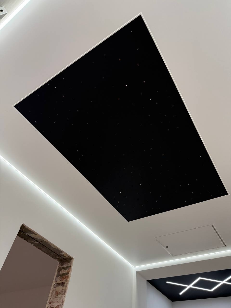 Nowoczesny sufit z efektem gwieździstego nieba i oświetleniem LED, widok z dołu. Fragment ściany z otworem drzwiowym w surowym stanie.
