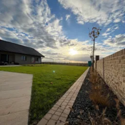 Nowoczesny ogród z równo przystrzyżonym trawnikiem, kamienną ścieżką i murem z cegły, oświetlony zachodzącym słońcem i dekoracyjnymi trawami.