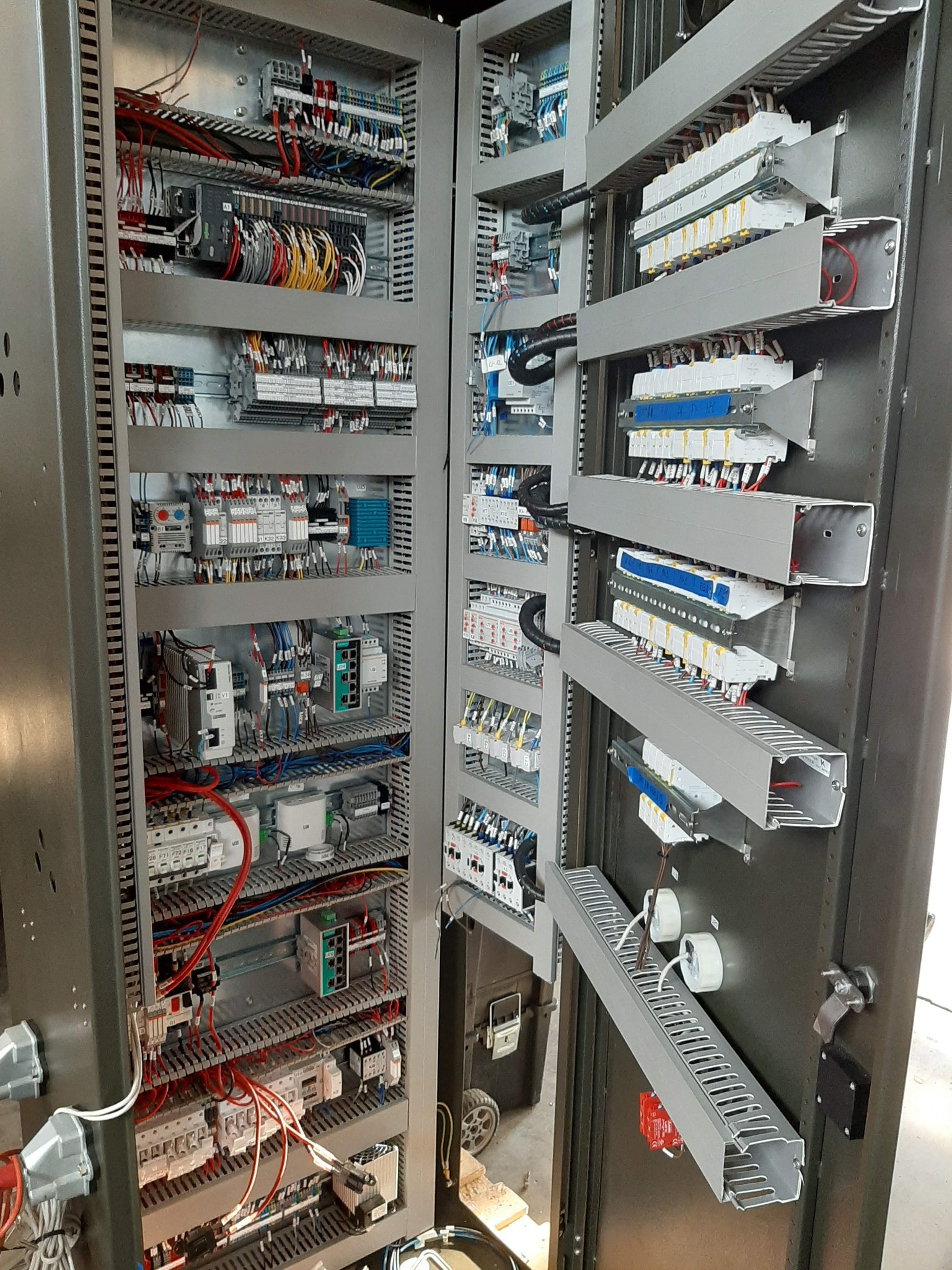 Otwarta szafa sterownicza z precyzyjnie ułożonymi kablami, bezpiecznikami i elementami automatyki. Widoczne listwy montażowe i okablowanie w różnych kolorach.