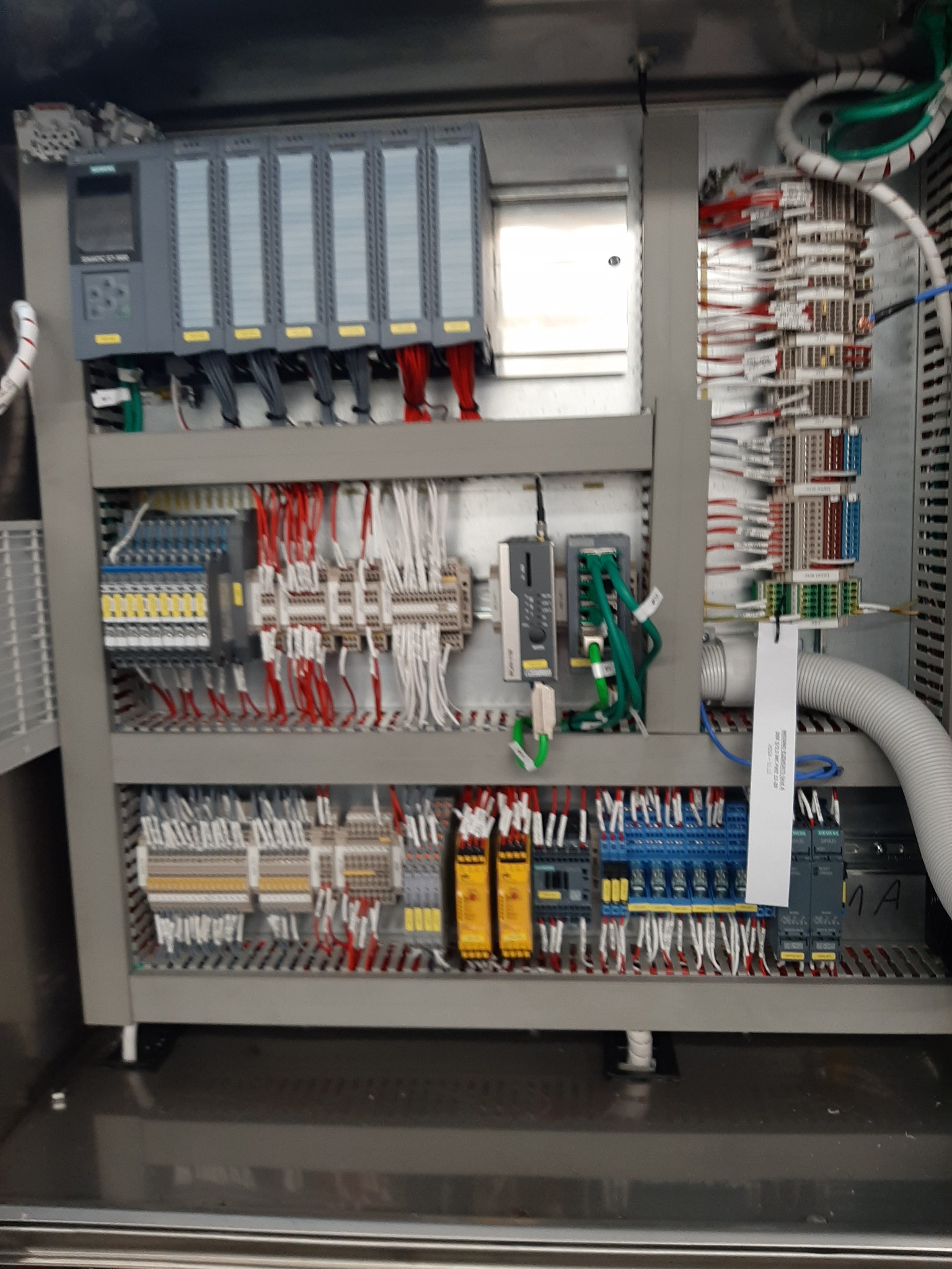 Rozdzielnica elektryczna z modułami Siemens, okablowaniem i elementami sterującymi w szarej obudowie. Widoczne przewody w różnych kolorach i oznaczenia.