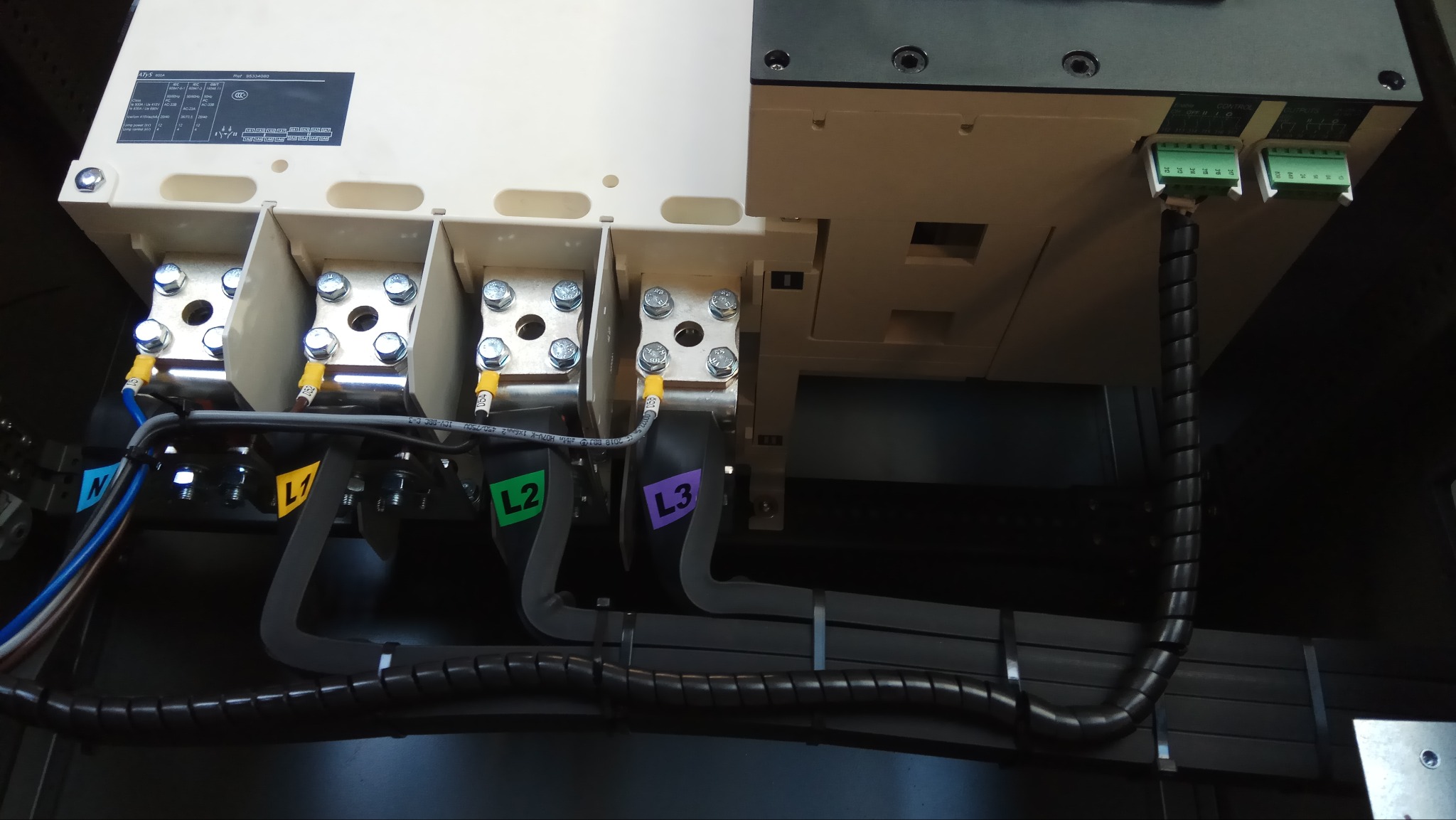 Rozdzielnica elektryczna z przewodami oznaczonymi kolorami L1, L2, L3 i N. Widoczne złącza i kable w peszlu. Szczegółowe ujęcie instalacji elektrycznej.