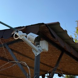 KARACA LIMITED - Kamera monitoringu Hikvision zamontowana na zadaszeniu w Warszawie. Widok z dołu, niebieskie niebo w tle. Zabezpieczenia i ochrona w zasięgu wzroku.