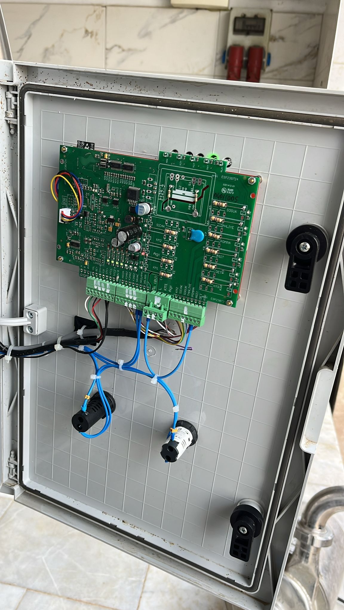 Otwarta skrzynka elektryczna z płytką drukowaną, widoczne kable i złącza. Element instalacji elektrycznej w szarej obudowie z tworzywa, z bliska.