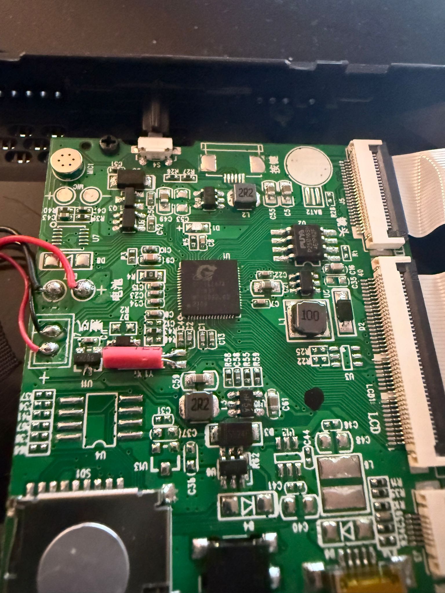 Zbliżenie na zieloną płytkę drukowaną z elementami elektronicznymi, takimi jak kondensatory, rezystory i układy scalone. Widoczne są także złącza i przewody.