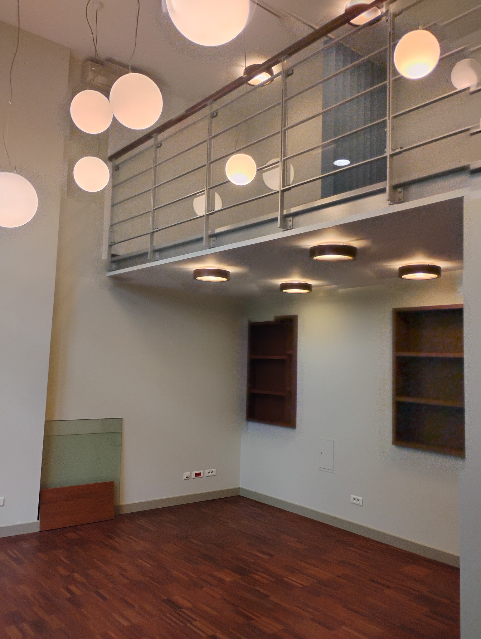 Puste, jasne wnętrze z drewnianą podłogą, antresolą z metalową barierką i kulistymi lampami. Na ścianach półki wnękowe. Widoczne gniazdka elektryczne.