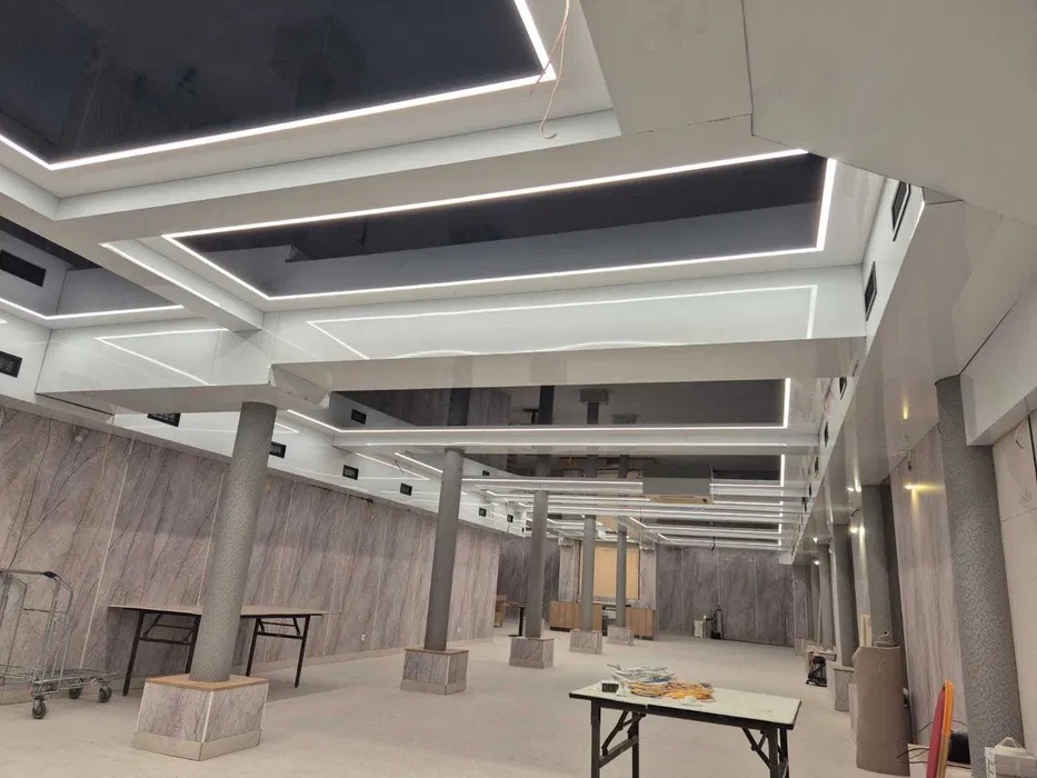 Nowoczesny sufit z podwieszanymi panelami i oświetleniem LED w lokalu. Widoczne kolumny i marmurowe ściany. Białe elementy konstrukcyjne.