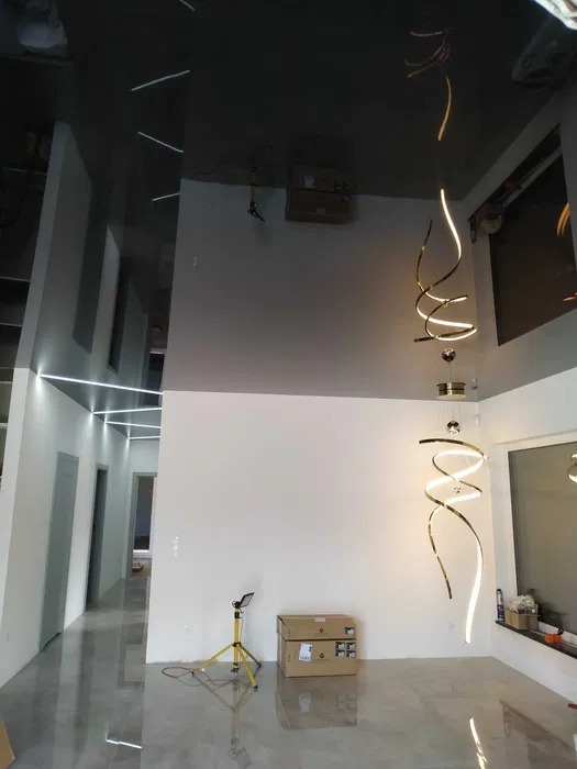 Nowoczesne wnętrze z błyszczącą, szarą podłogą i podwieszanym sufitem z liniowym oświetleniem LED. Spiralna lampa zwisa w przestronnym pomieszczeniu.