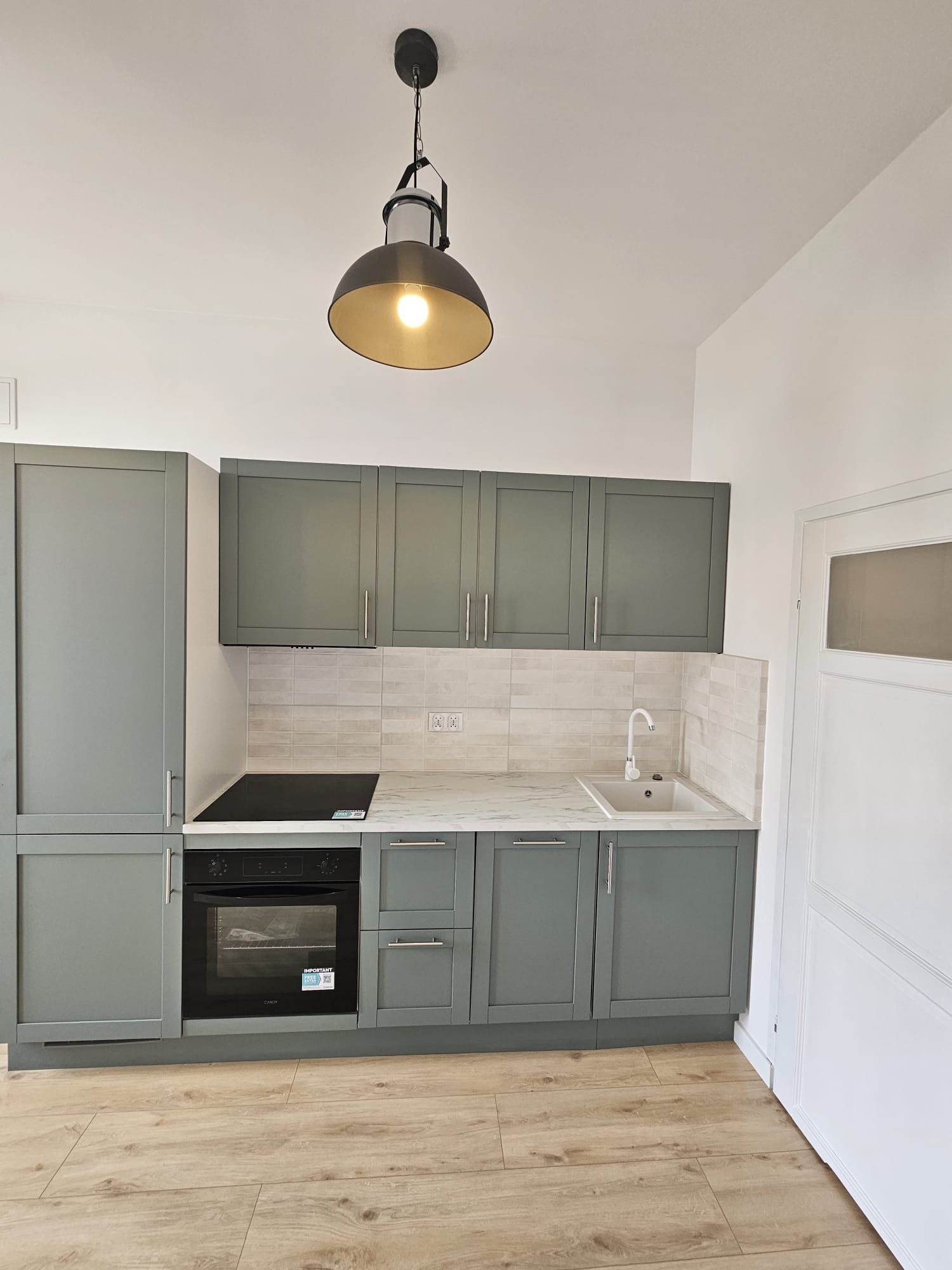 Nowoczesna kuchnia w odcieniach szarości z drewnianą podłogą i lampą w stylu industrialnym. Uwagę przykuwają minimalistyczne fronty szafek i marmurowy blat.