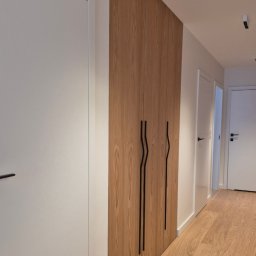 ARCHIDOM MARIUSZ SZKUTAK - Zabudowa z forniru dębowego w przedpokoju, z czarnymi, niestandardowymi uchwytami. Rytmiczny układ frontów współgra z podłogą, tworząc spójną, elegancką przestrzeń.