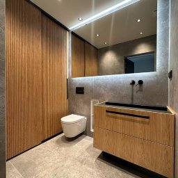 ARCHIDOM MARIUSZ SZKUTAK - Nowoczesna łazienka: ryflowane drzwi przesuwne, fornirowana szafka pod umywalkę, podwieszana toaleta, duże lustro z podświetleniem LED i ciemna armatura.