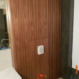 ARCHIDOM MARIUSZ SZKUTAK - Zabudowa WC z forniru orzechowego z ryflowanym panelem w trakcie realizacji. Widoczne elementy instalacji i sterownik. Nowoczesny, uporządkowany projekt łazienki.