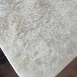 ARCHIDOM MARIUSZ SZKUTAK - Jasny blat z kwarcytu Taj Mahal z zaokrąglonym rogiem, na którym stoi czarny kubek. Widoczny fragment podłogi i buta.