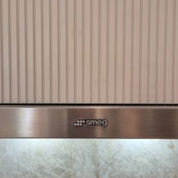 Ryflowany detal widoczny nad okapem Smeg to elegancki akcent, który przełamuje gładkie powierzchnie zabudowy kuchennej i dodaje jej subtelnej struktury. Idealnie komponuje się z kamiennym wykończeniem w tle, nadając całości wyjątkowego charakteru.