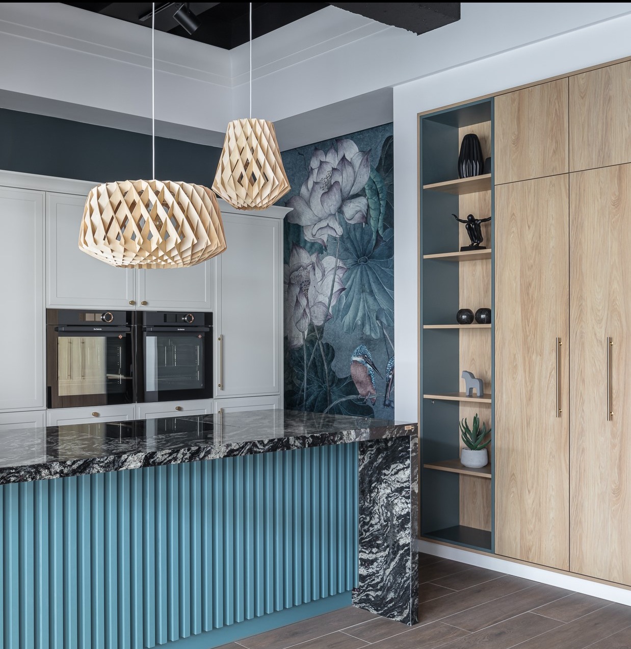Nowoczesna kuchnia z wyspą, granitowym blatem Sensa Cosentino, frontami z hikory i szmaragdowym panelem z lamelami. Dekoracyjna tapeta z motywem roślinnym.