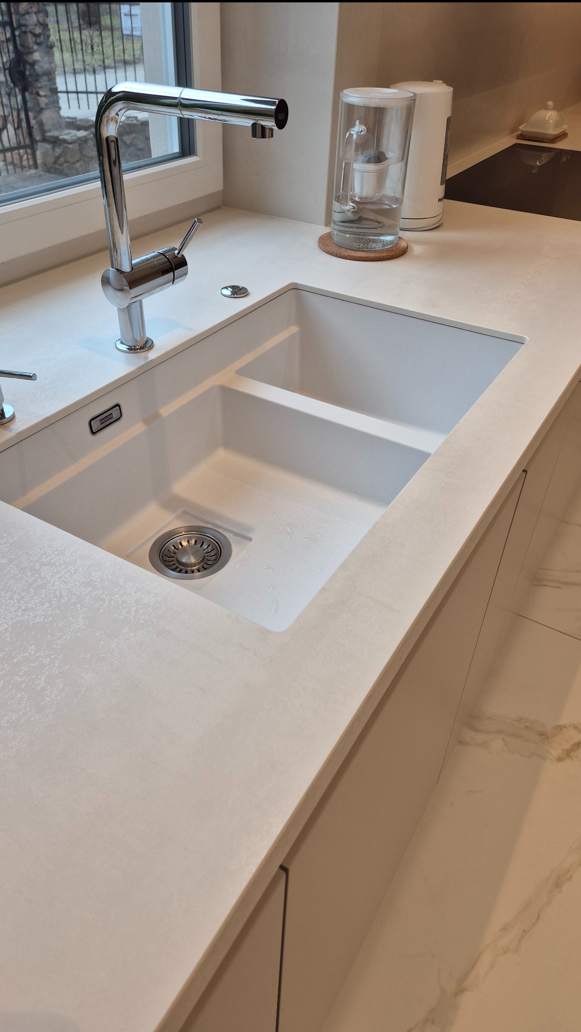 Jasny blat kamienny ze zintegrowanym zlewem Franke w kuchni w Krakowie. Nowoczesna bateria, filtr do wody i subtelny wzór spieku kwarcowego.